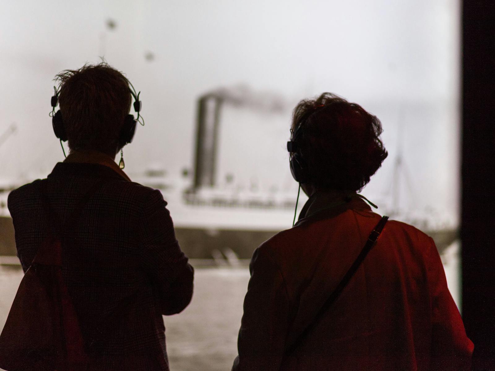 Two visitors onlook a photo while listening through guided headphones