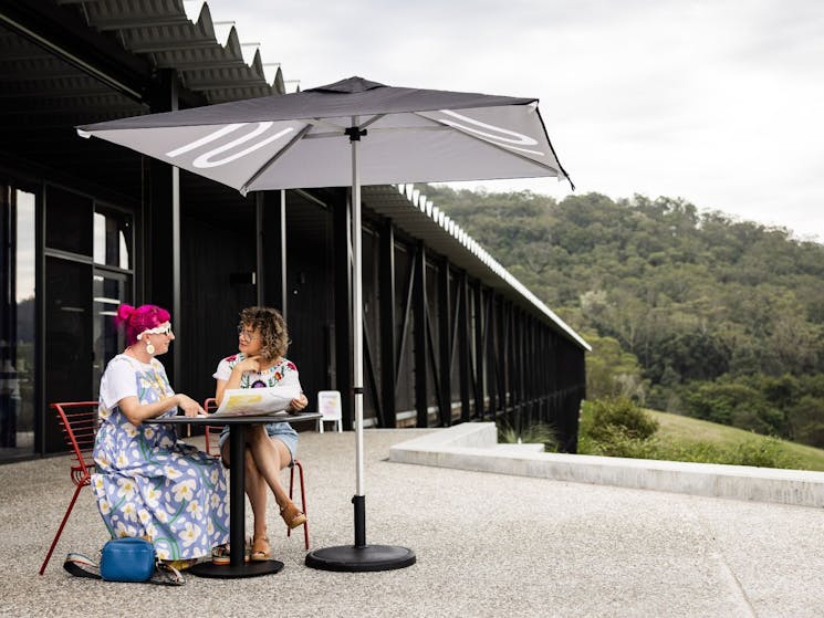 Two visitors sit outside Ramox Cafe at a table with a view along the length of The Bridge