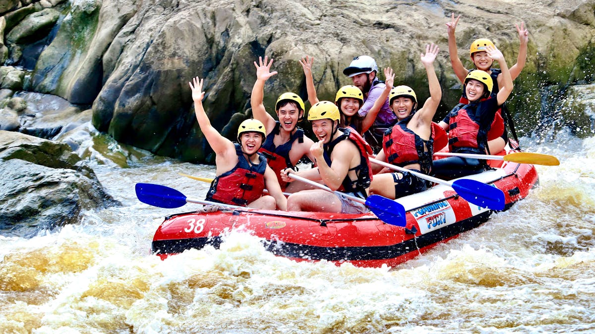 Group of 7 smiling and waving as they raft down the Barron River in the Barron Gorge National Park