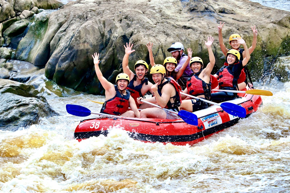 Group of 7 smiling and waving as they raft down the Barron River in the Barron Gorge National Park