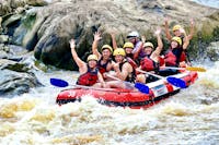 Group of 7 smiling and waving as they raft down the Barron River in the Barron Gorge National Park