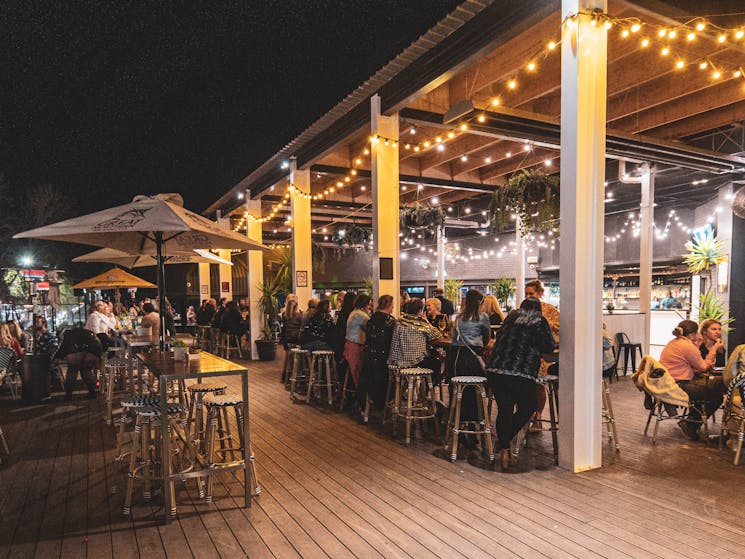 A night time photo of the Tilly's Deck area with people enjoying company of their friends at a table