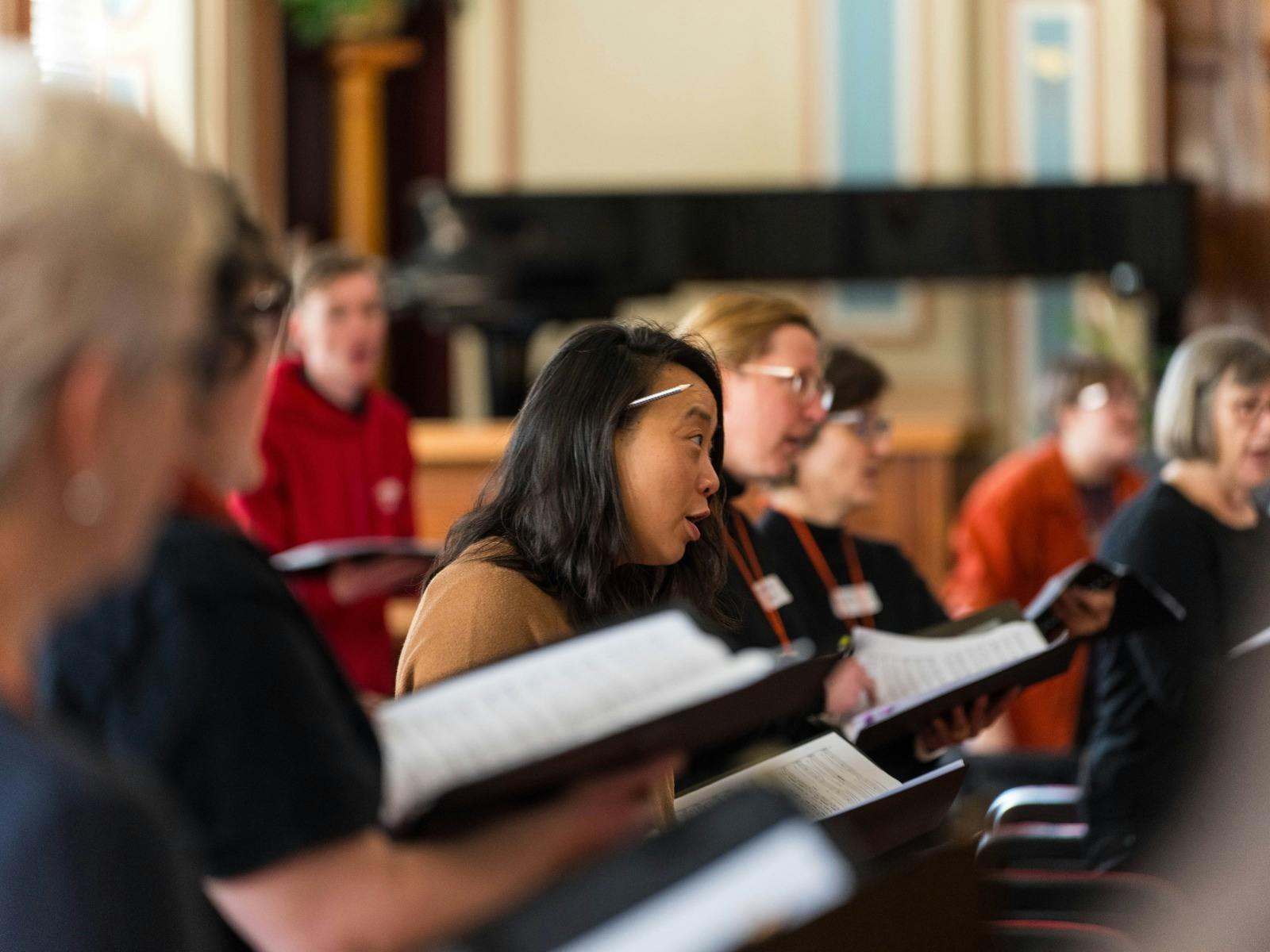 People holding music scores, focusing intently during a choral workshop.