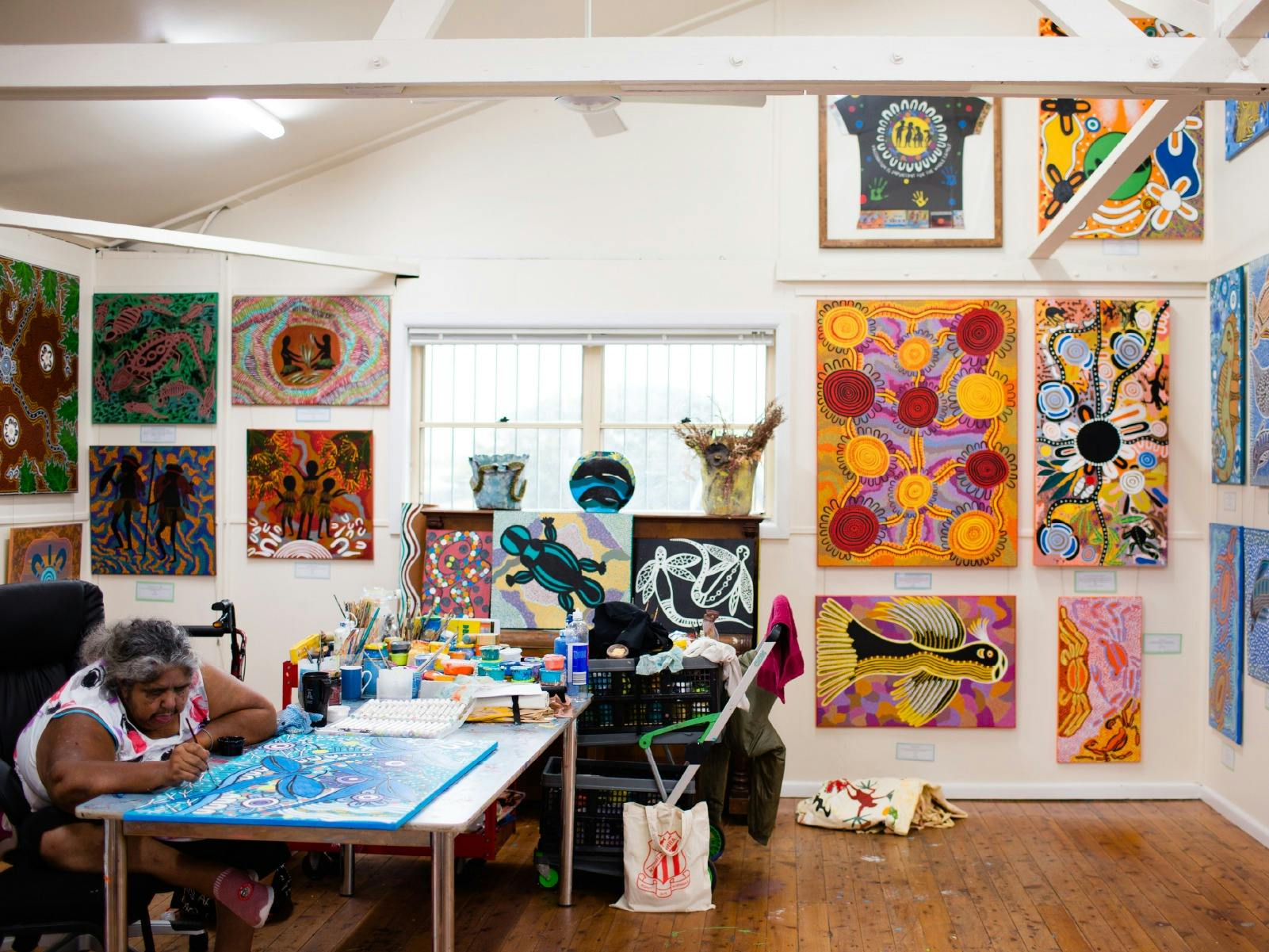 Woman painting in an exhibition space surrounded by painting and paint products