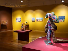 A wide shot of the gallery featuring brightly painted walls, wooden floorboards and soft sculptures