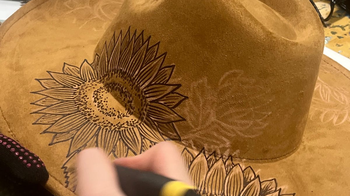 A person with a hat burning tool bruning their art onto a hat