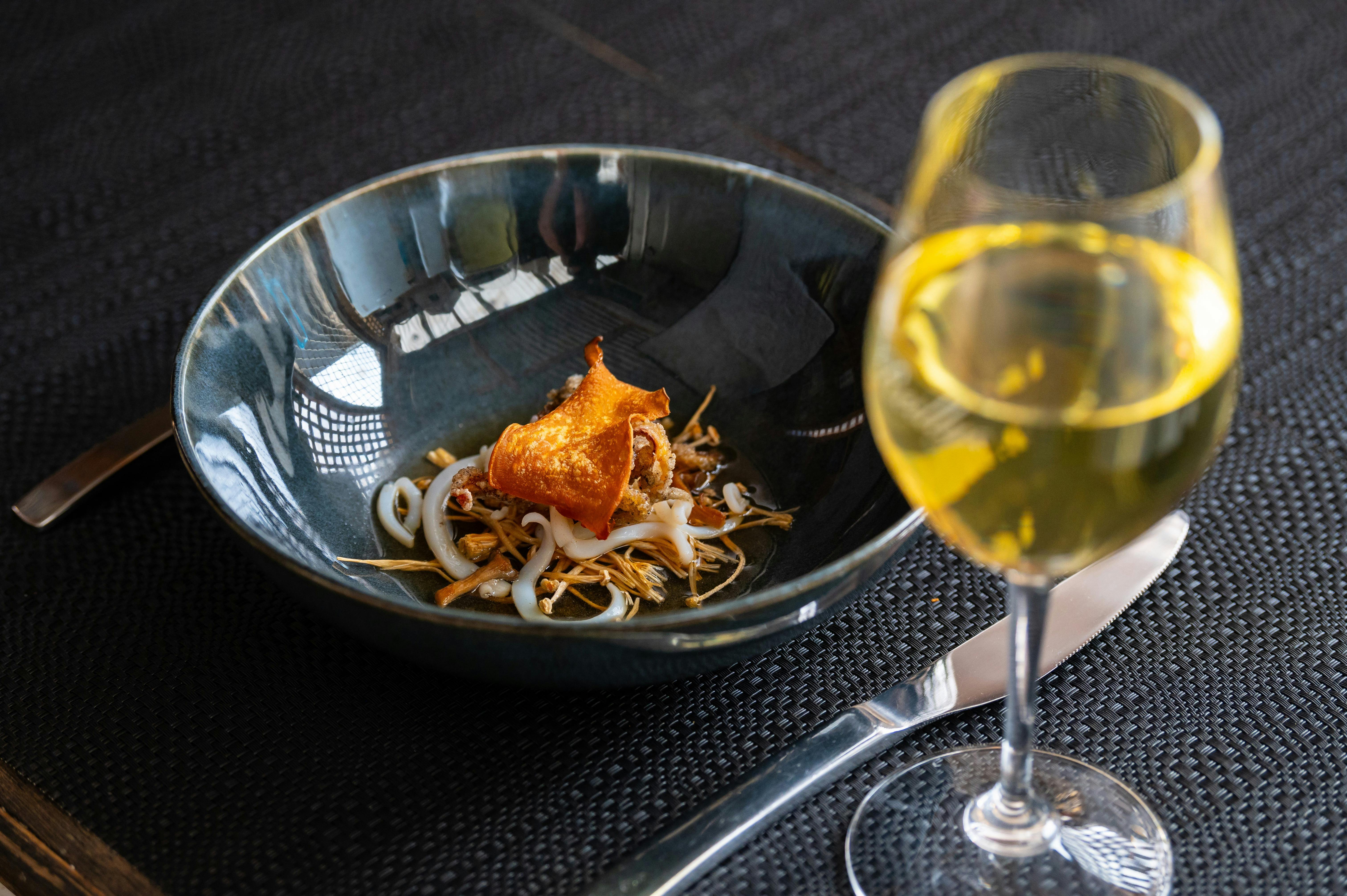 Gourmet squid entree in dark bowl behind glass of premium Reillys Watervale Aged Riesling