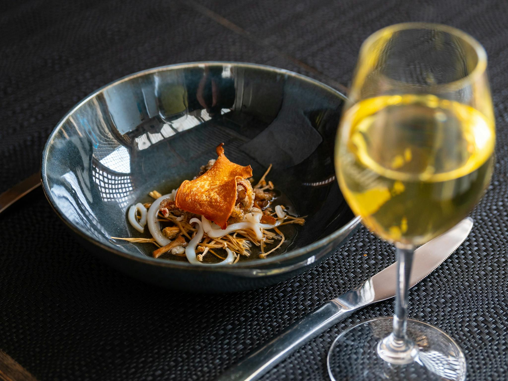 Gourmet squid entree in dark bowl behind glass of premium Reillys Watervale Aged Riesling