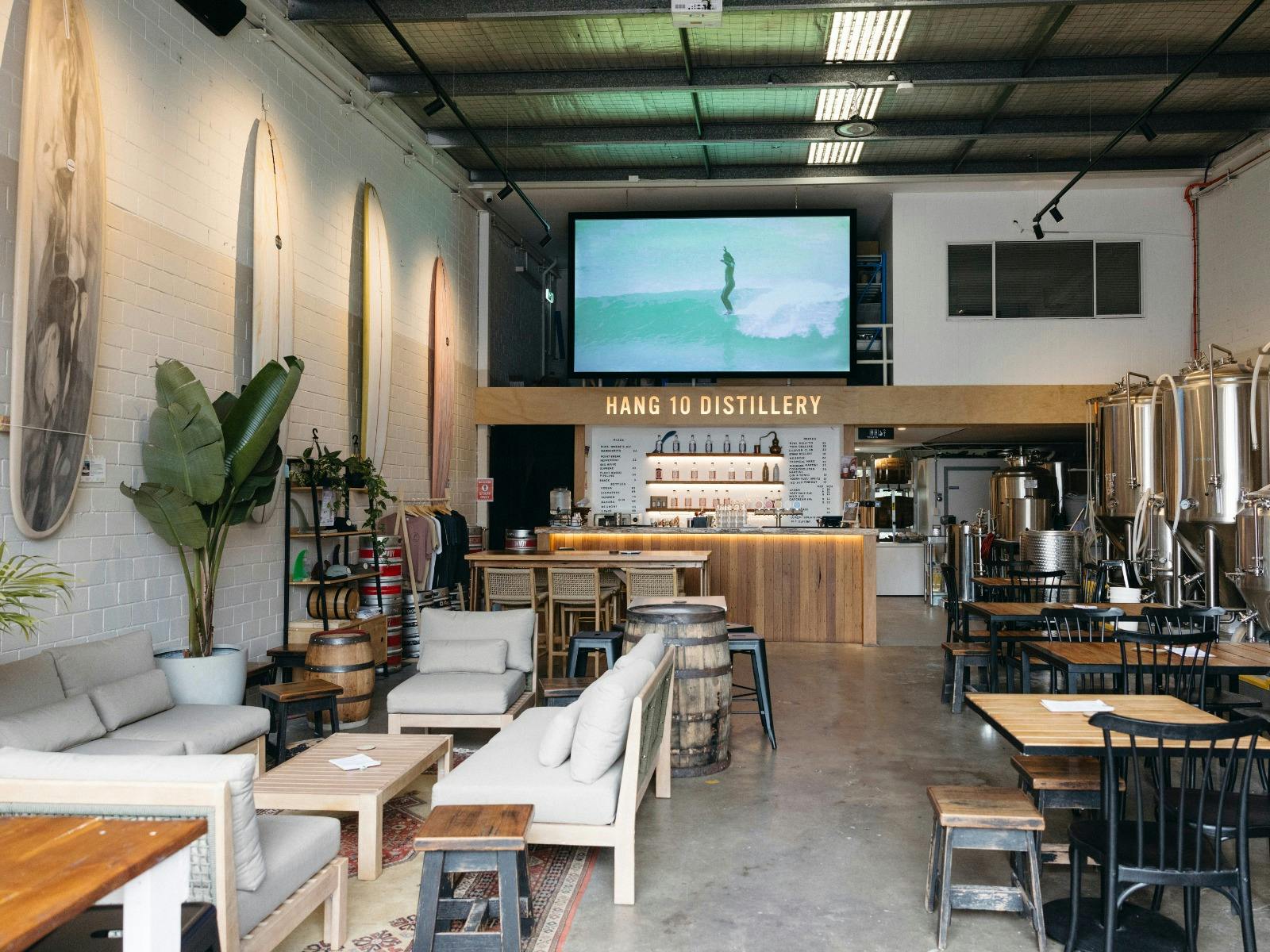 The interior of Hang 10 Distillery with a couch area, tables, a bar and a big screen playing a video
