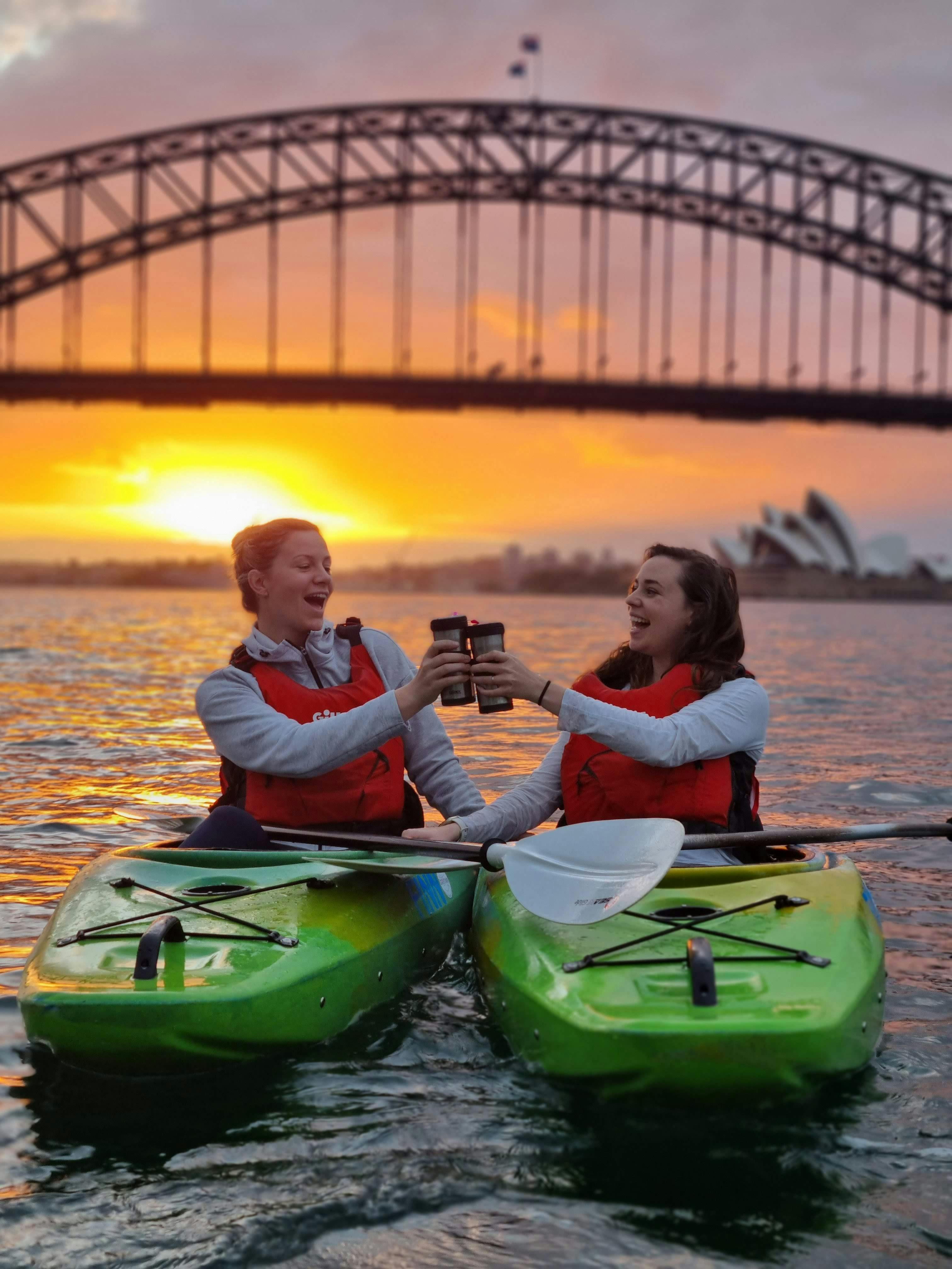 シドニー港の日の出を眺めながら、カヤックからコーヒーを楽しむ女性2人。