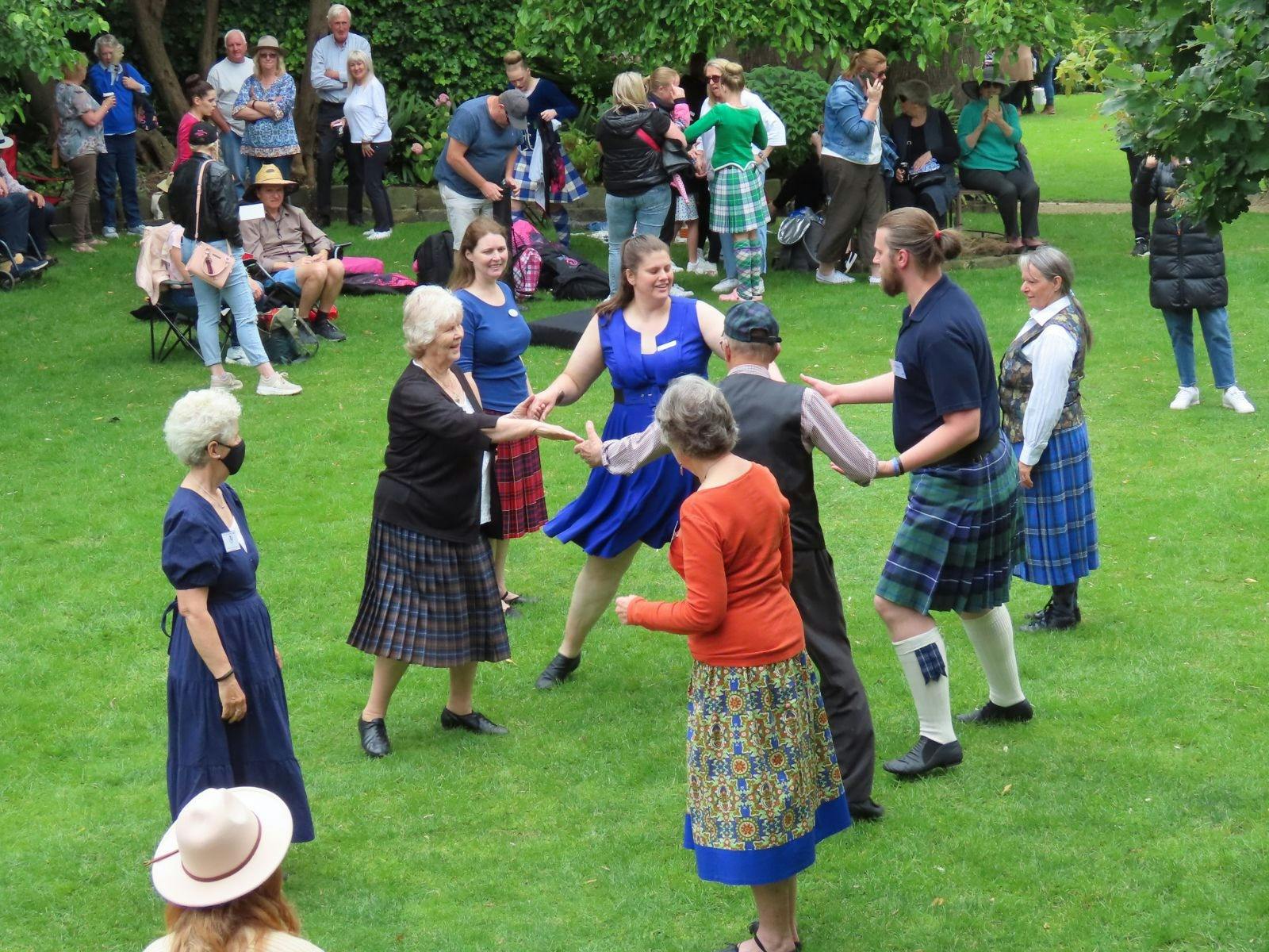 Various people dancing on a green lawn, they are different ages, while people watch
