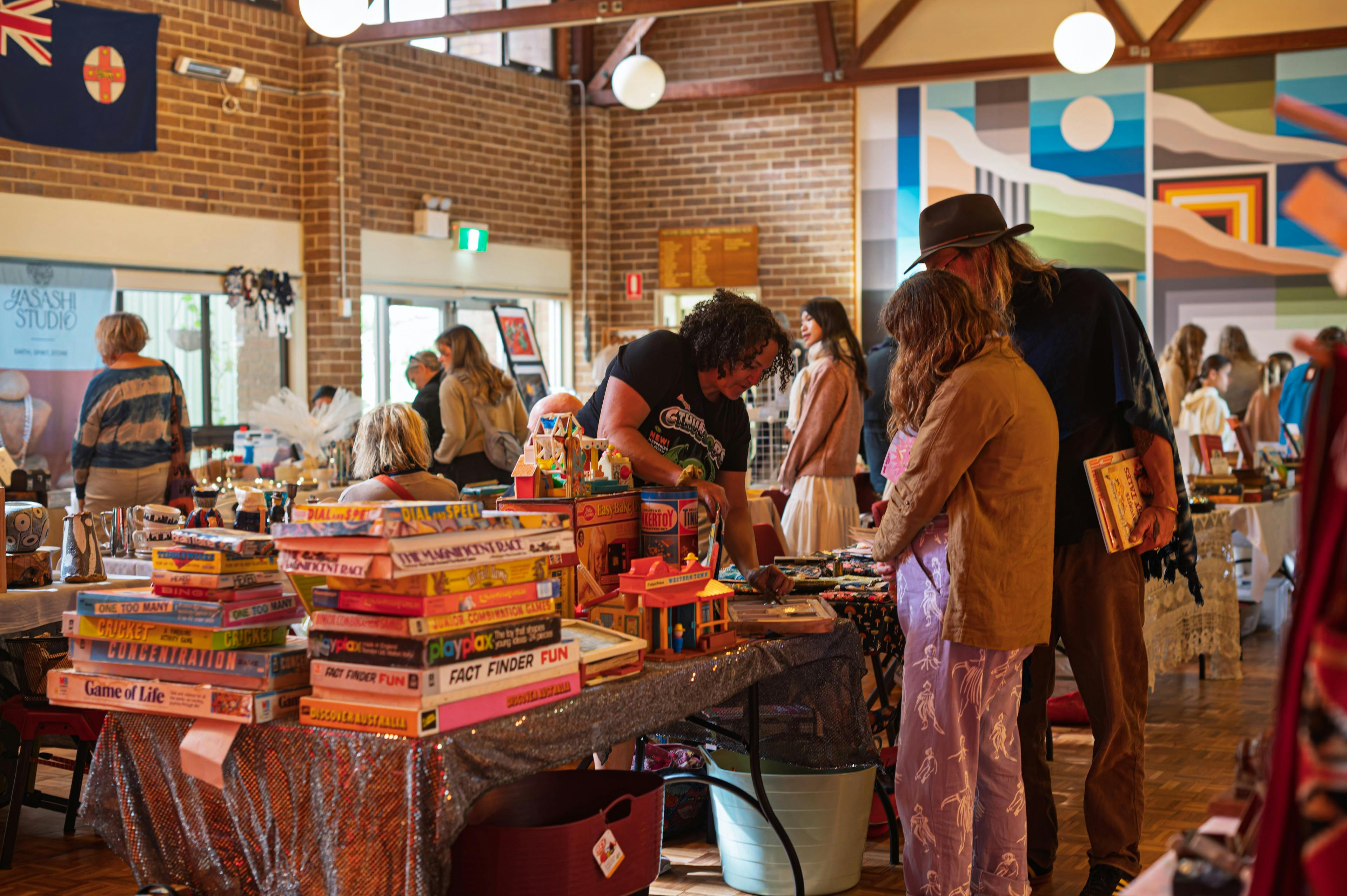 People talking across a market table full of vintage games. Other people are in the background.