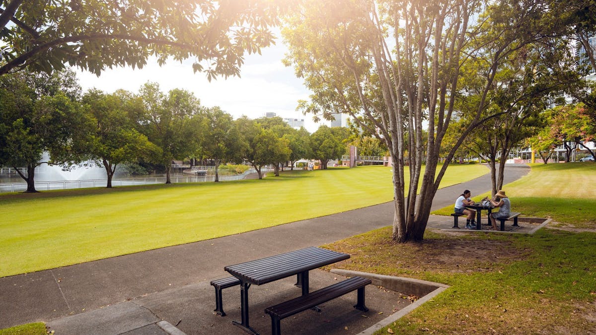 Tree lined lawn with two picnic tables overlooking a lake