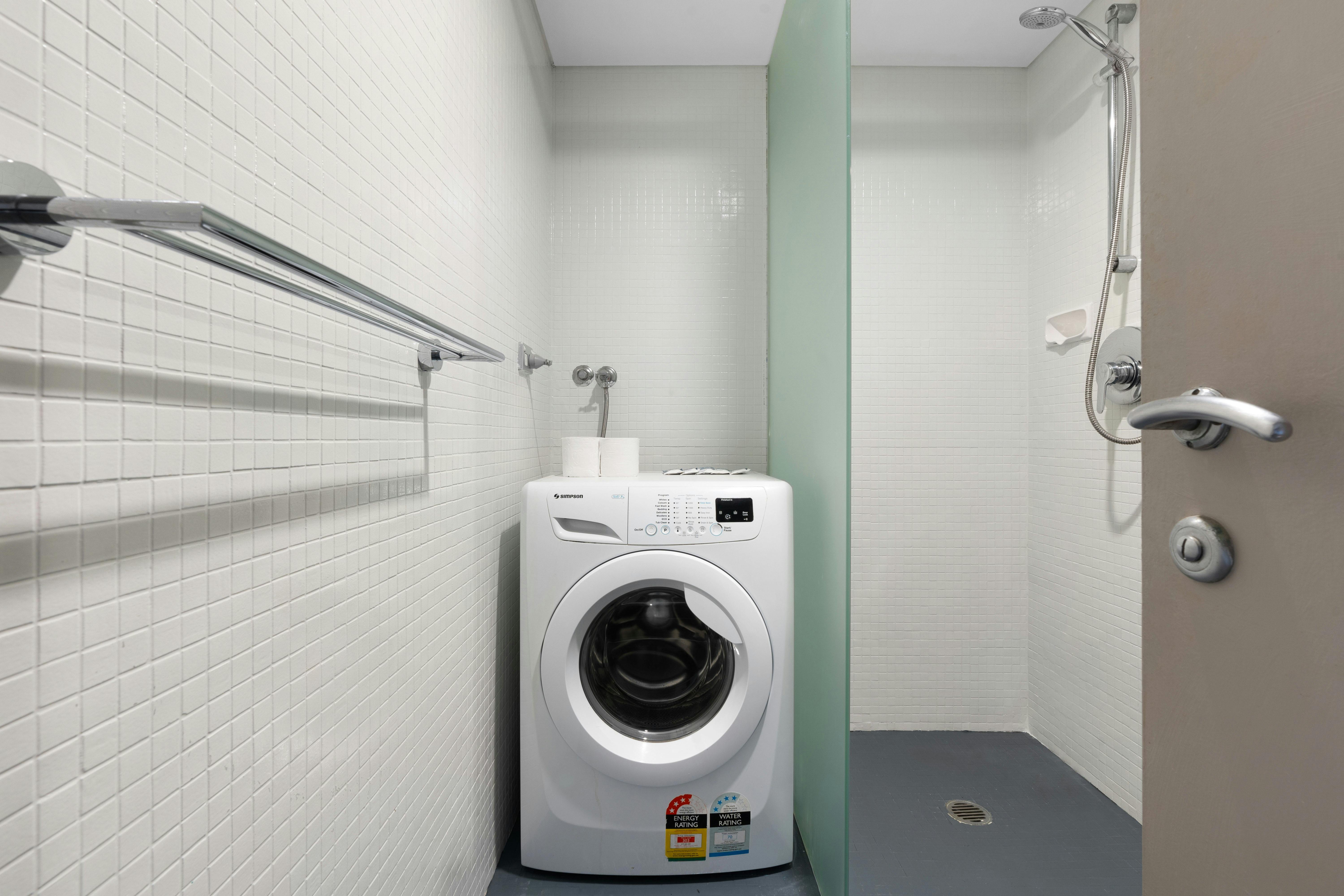 現代化的瓷磚空間內設有緊湊型洗衣房，配有洗衣機、淋浴和毛巾架。