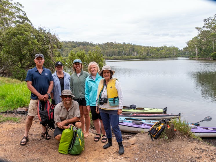 Group poses next to river for photo with kayaks and Bermagui River in the background