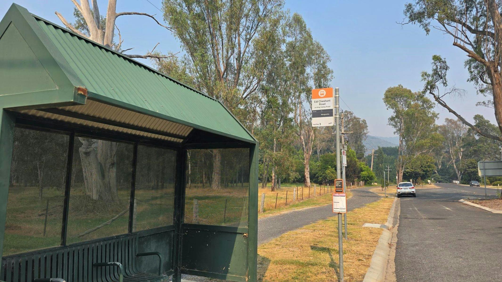 Green bus stop in front of a bus stop sign and blue skies
