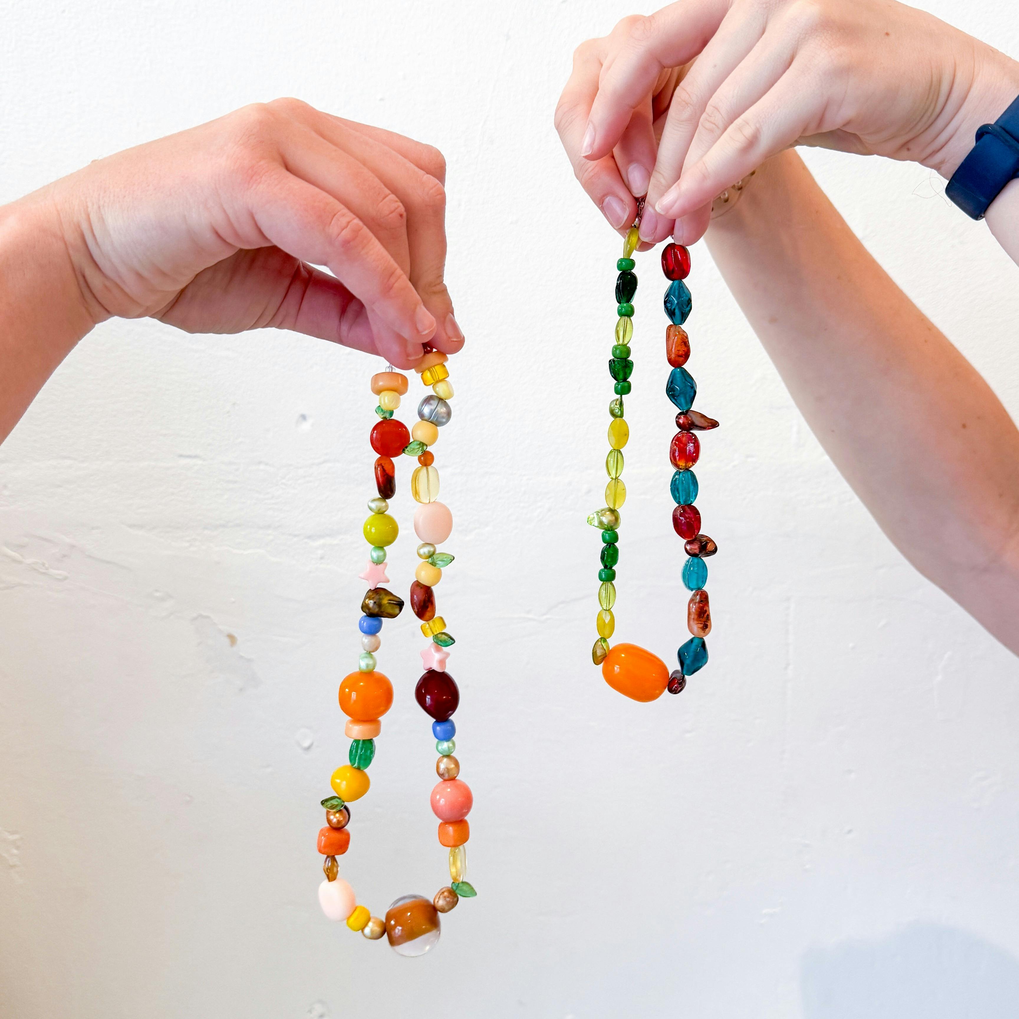 Two hands holding colourful beaded necklaces