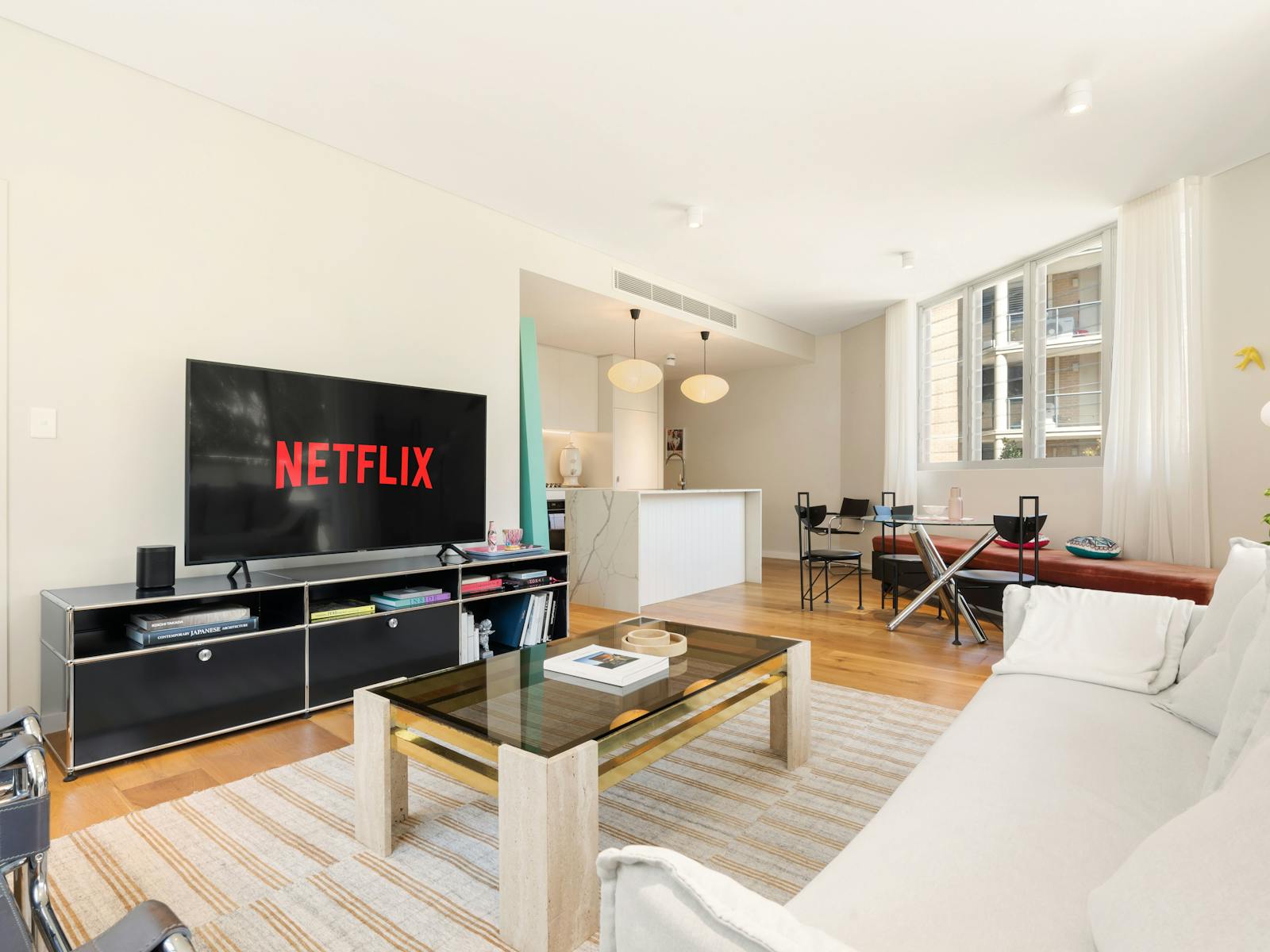 Living room with stylish chairs, a sofa, and large windows bringing in sunlight.