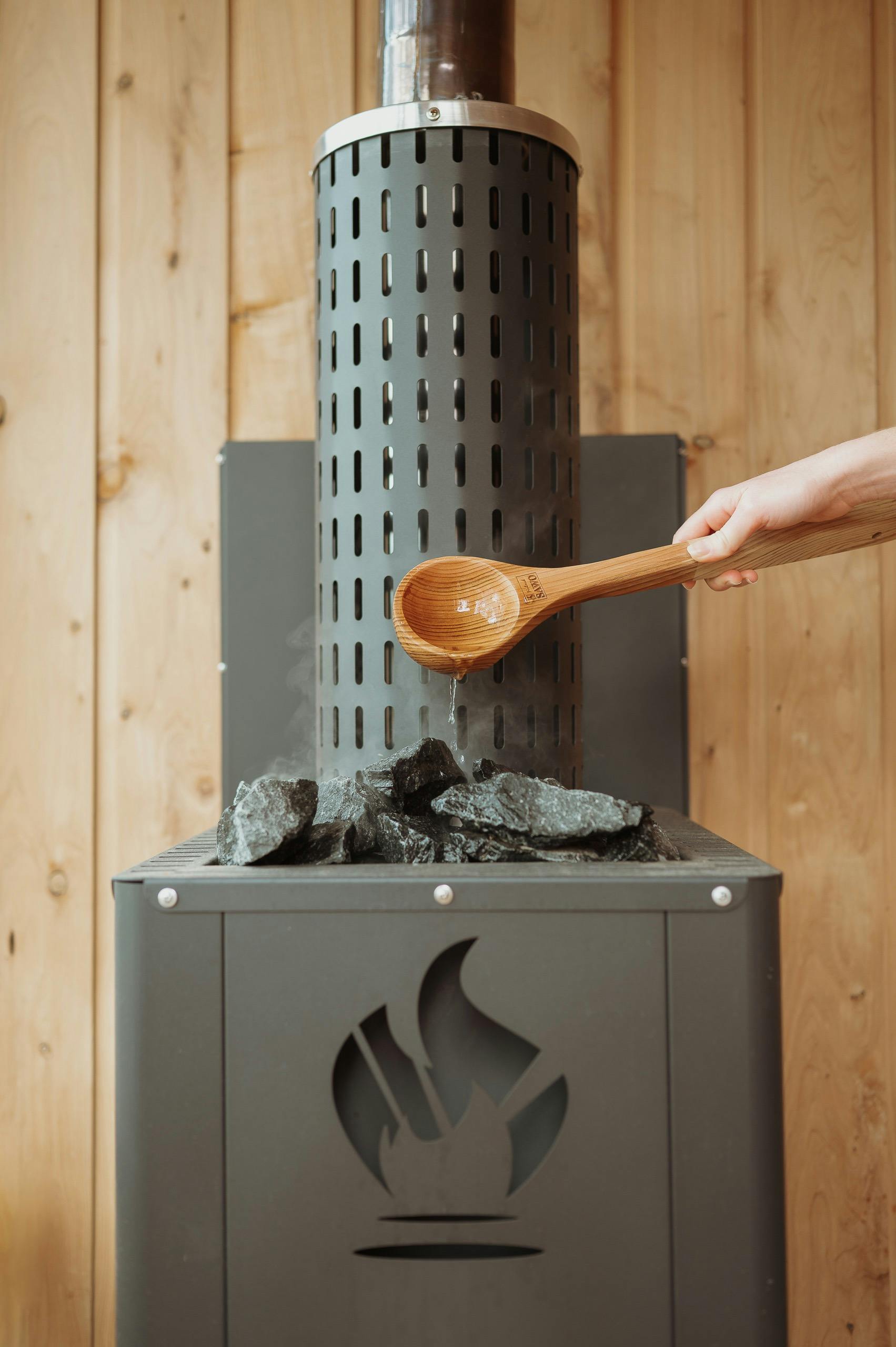 Wooden ladle spooning water on coals in sauna