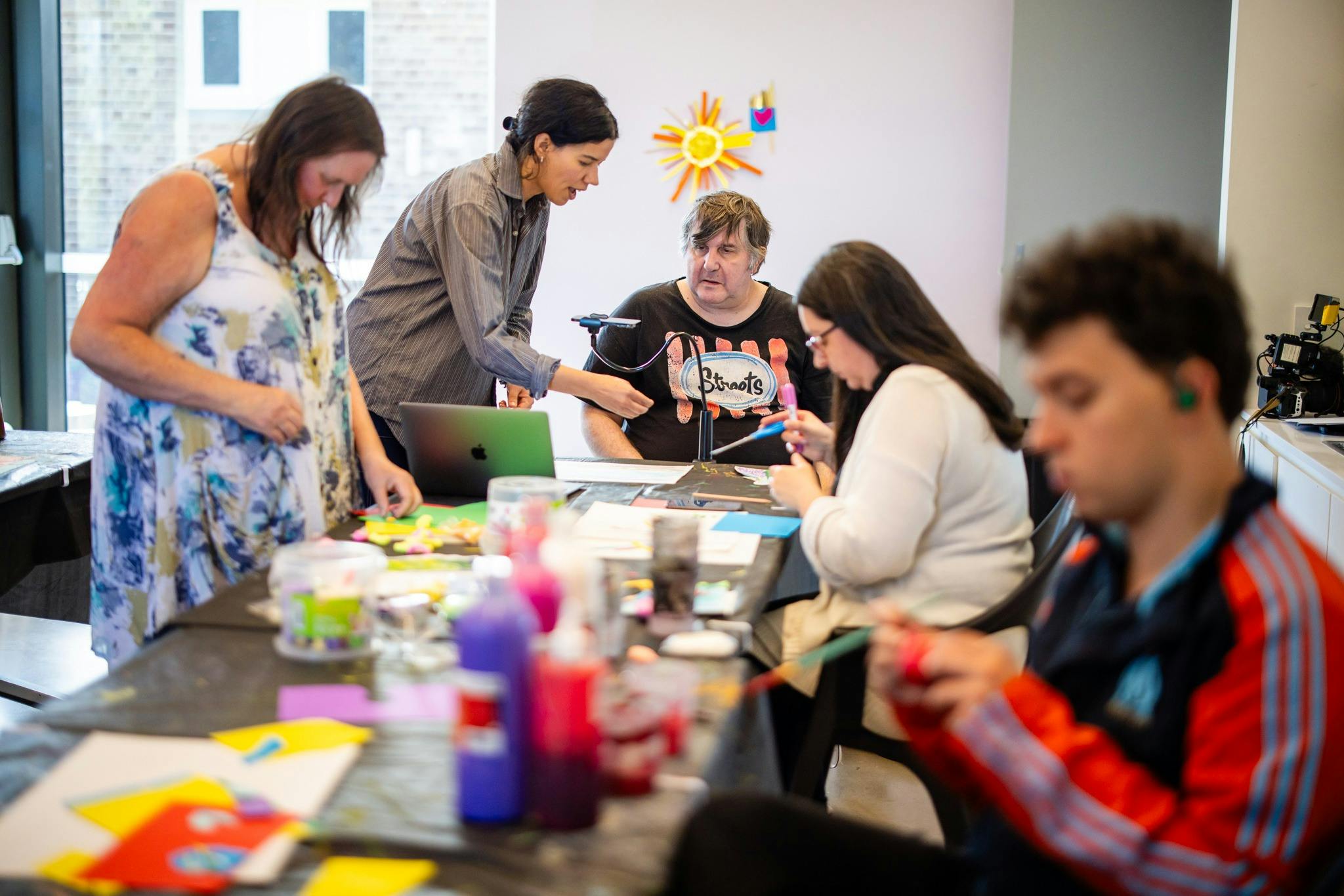 a group of people gather around talking and making in an art room