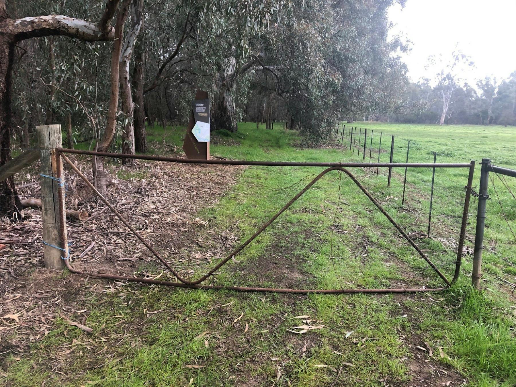 Rusty farm gate, green grass, directional signage, fence, paddock, river red gums in background