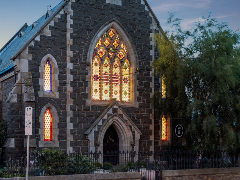 historic bluestone church at dusk, with stained glass windows lit from within
