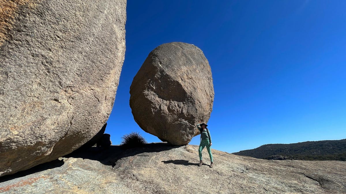 Woman standing next to huge egg shaped boulders on a a granite rock surface