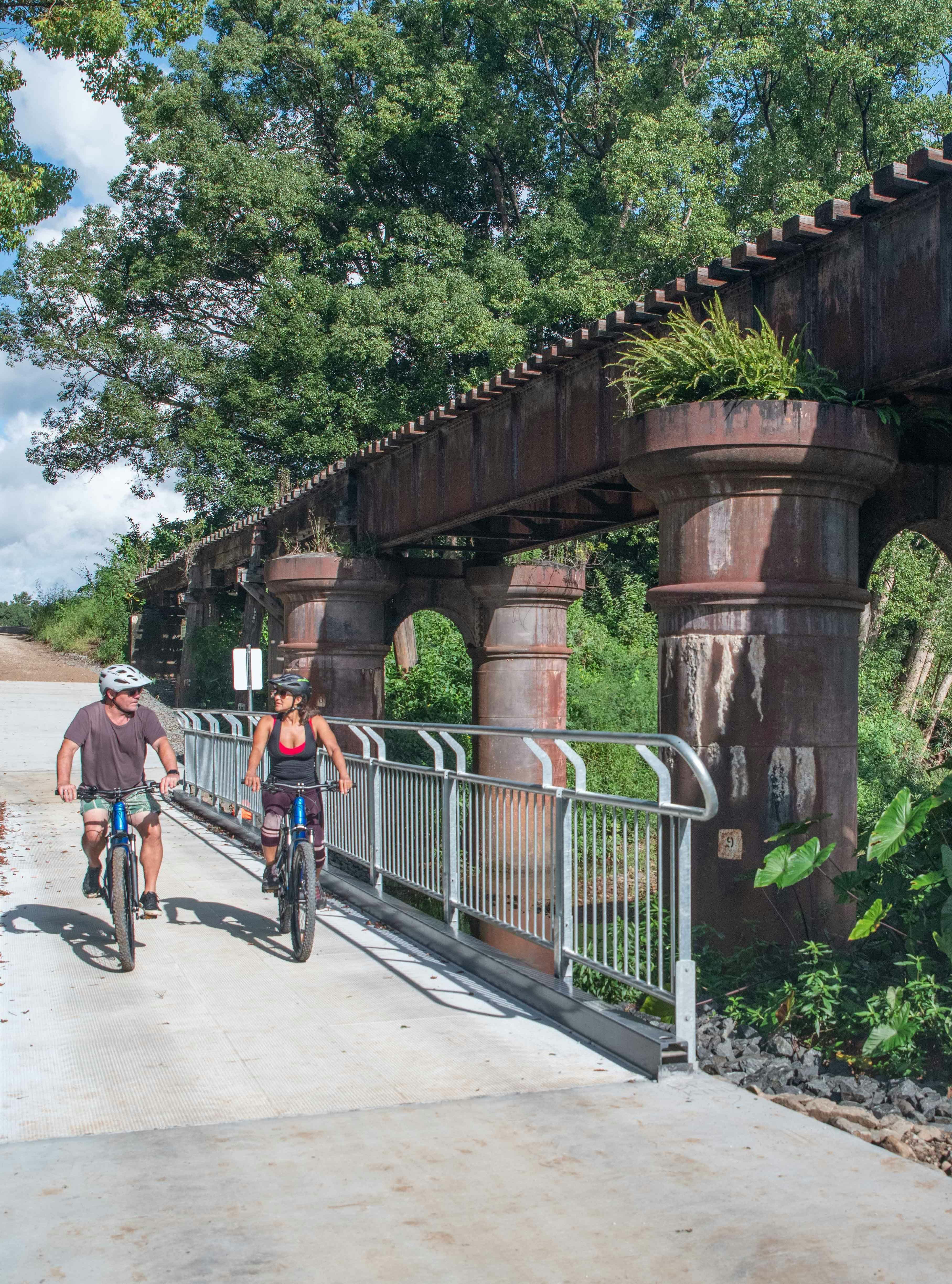 Two people on e-bikes riding past an old railway bridge