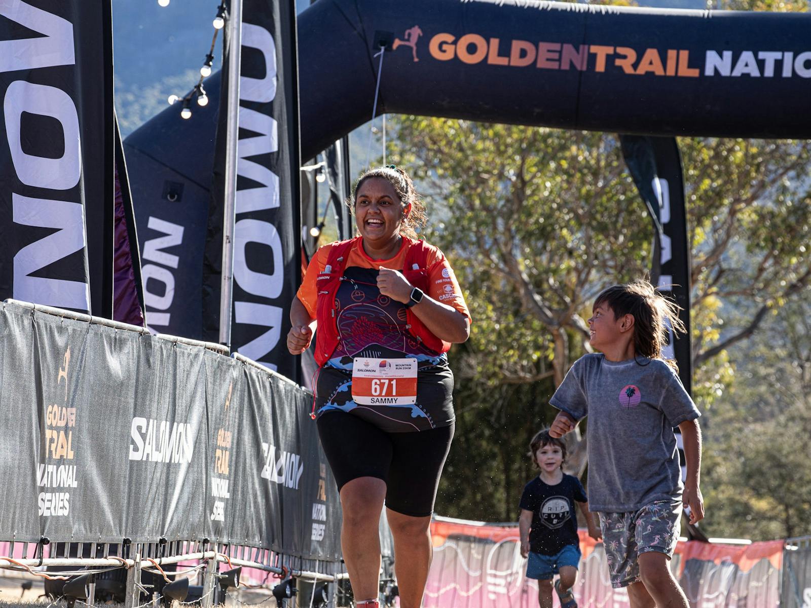 A woman runs through the finish arch with children next to her
