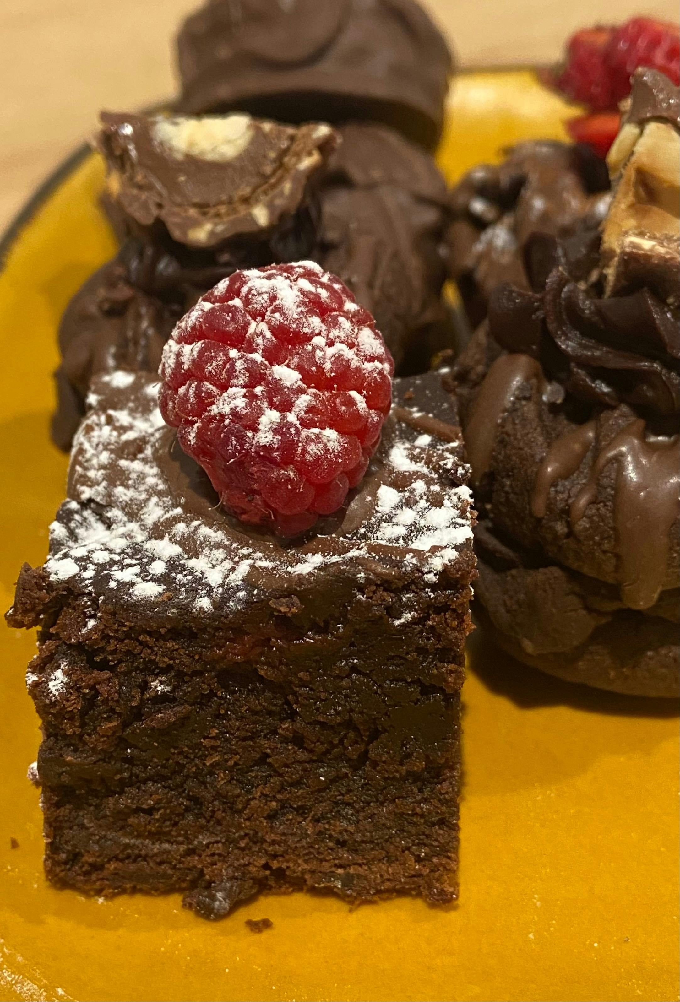 A plate of chocolate brownies with raspberries on top