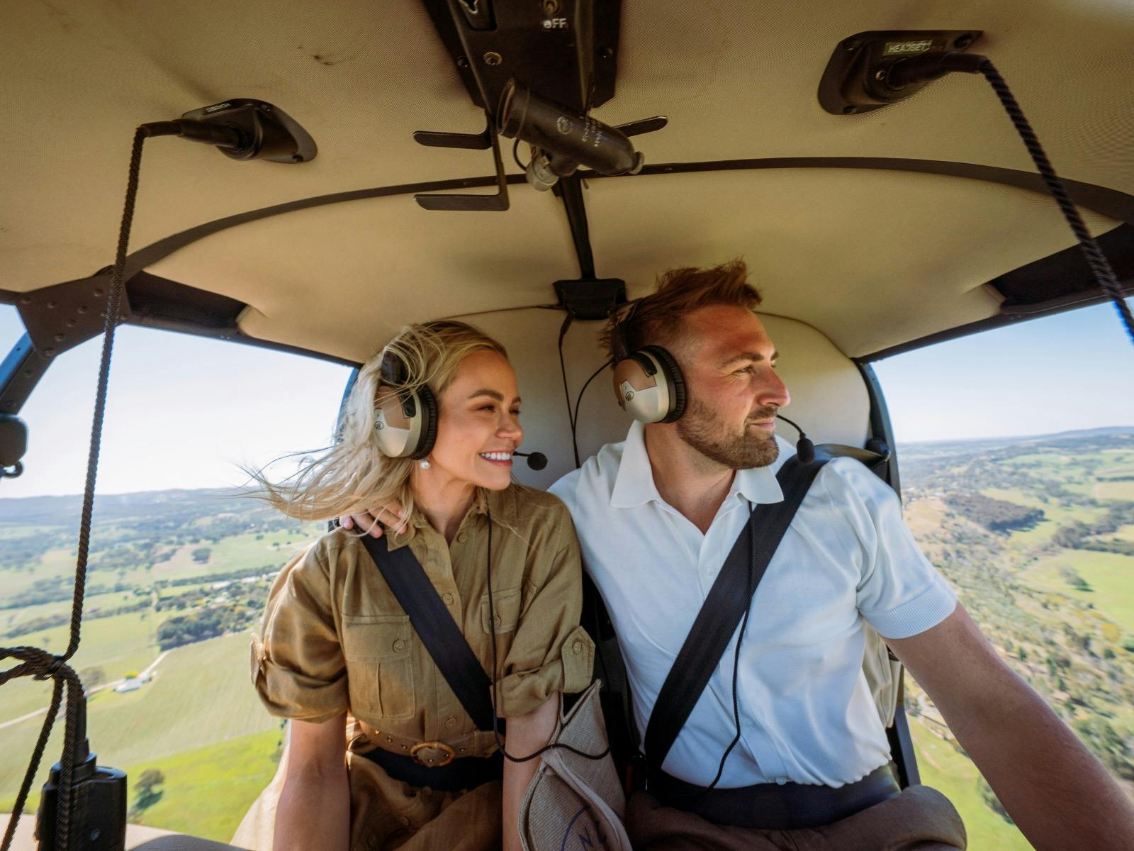 A happy smiling couple is sitting inside the helicopter, flying over the South Australian landscape.
