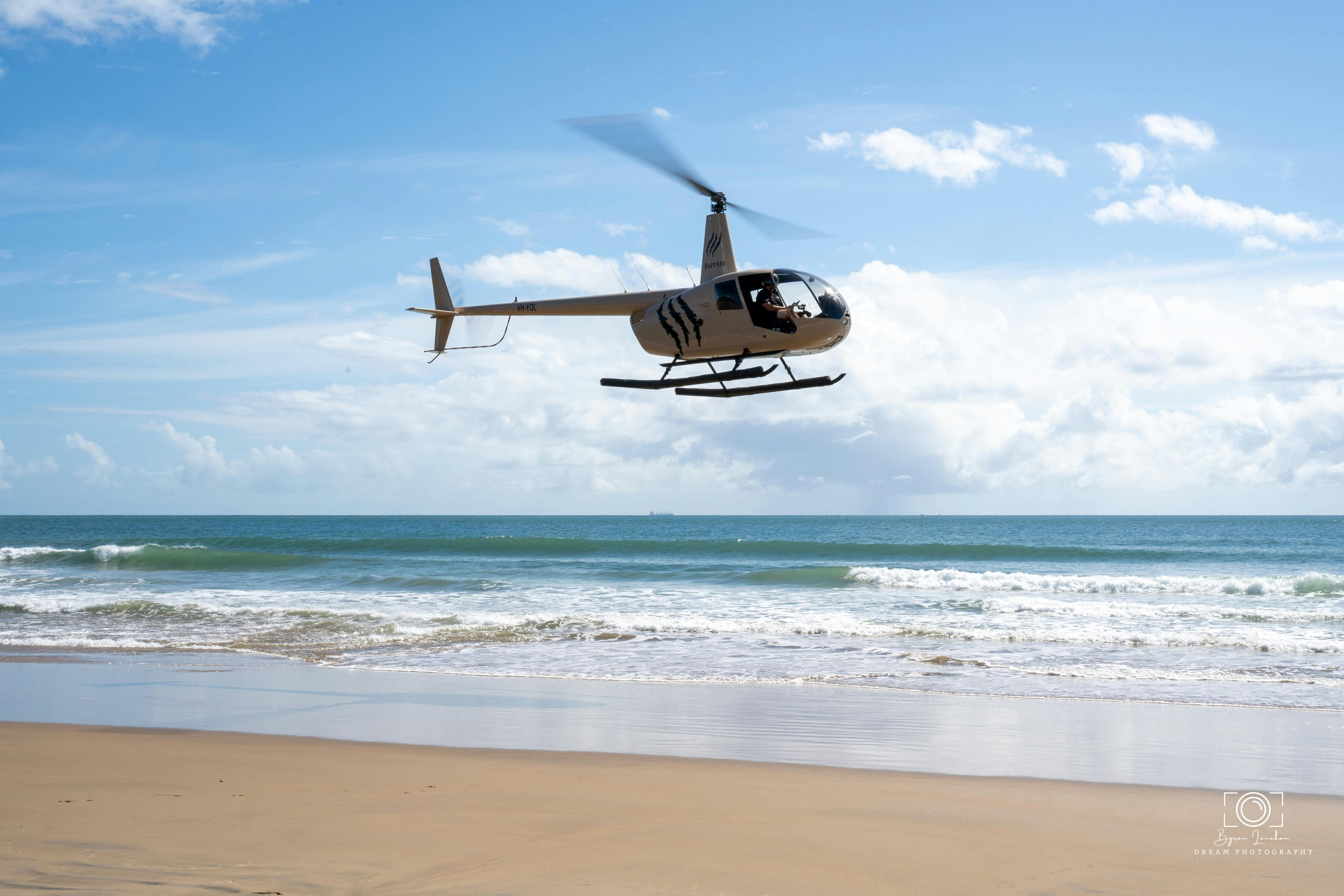 the RaptAir helicopter flying low over beautiful sandy beach and turquoise gentle surf