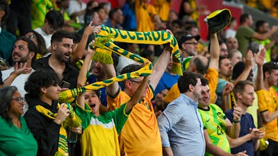 Soccer players in yellow kits celebrate a goal on a stadium pitch as teammates run in behind