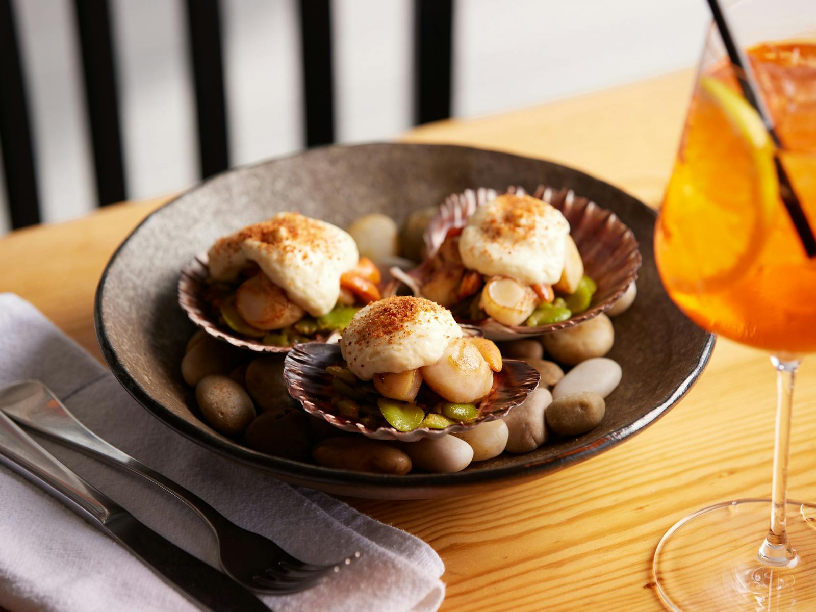 Scallops presented in three scallop shells, with smashed broad beans and a xo scallop bacon cream