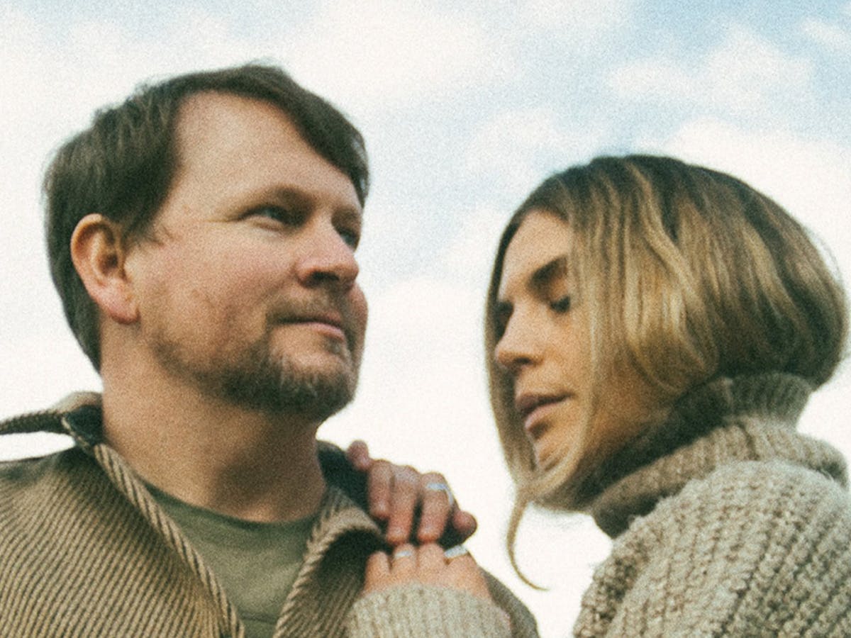 A close-up photo of a man and a woman standing outdoors under a cloudy blue sky.