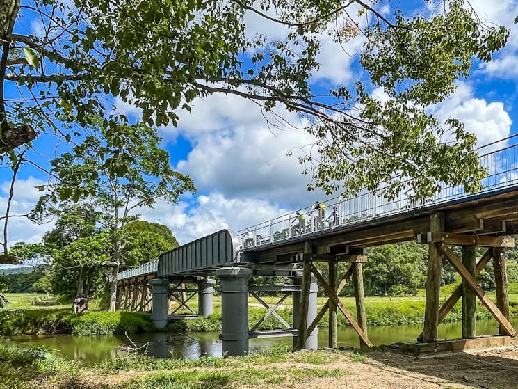 Side view of old railway bridge with e bike riders at mooball on the Northern Rivers Rail Trail