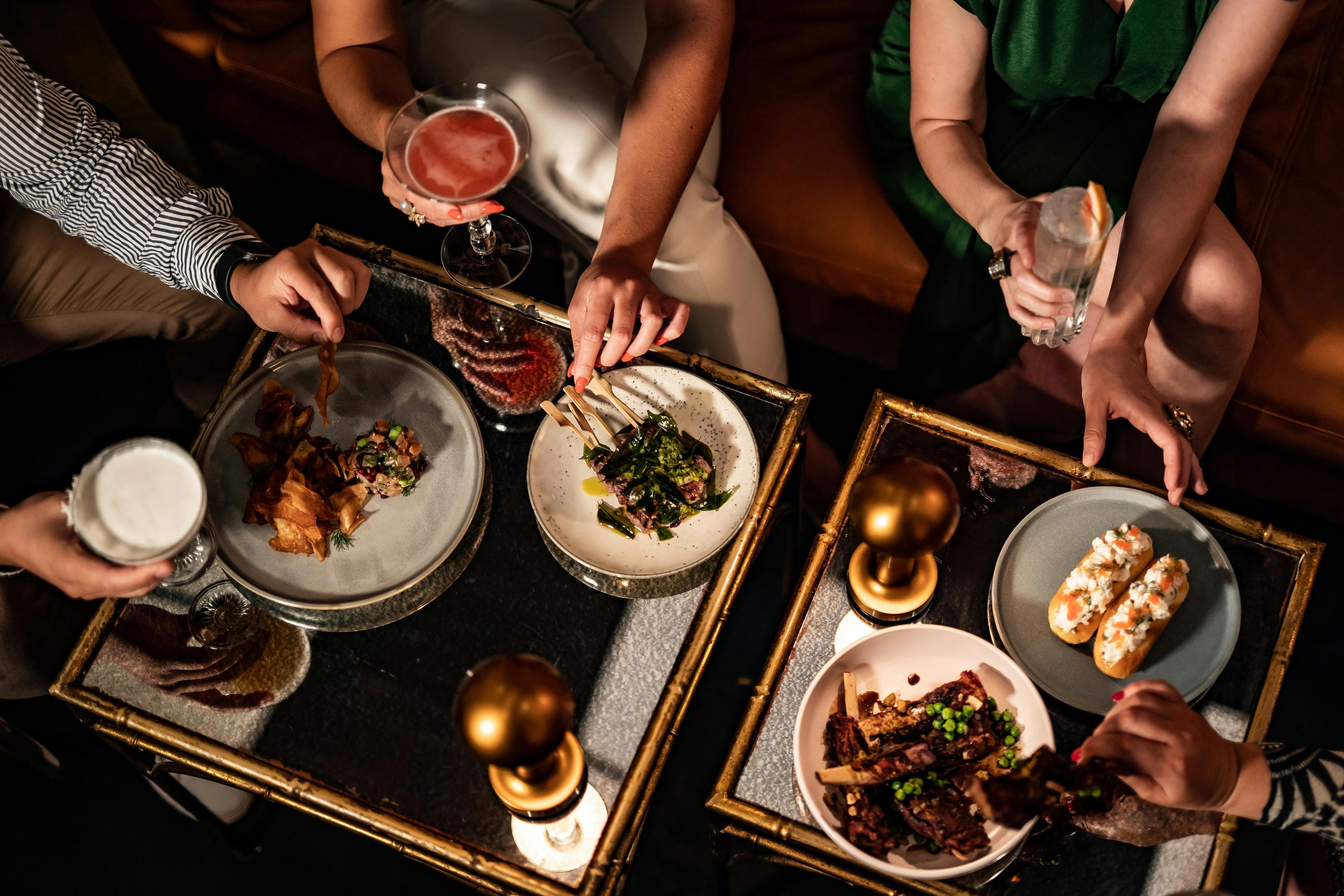 A table with food and cocktails and people eating and drinking with their hands