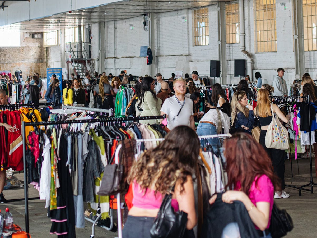 pictured is a view of the market with lots of racks of clothes and people