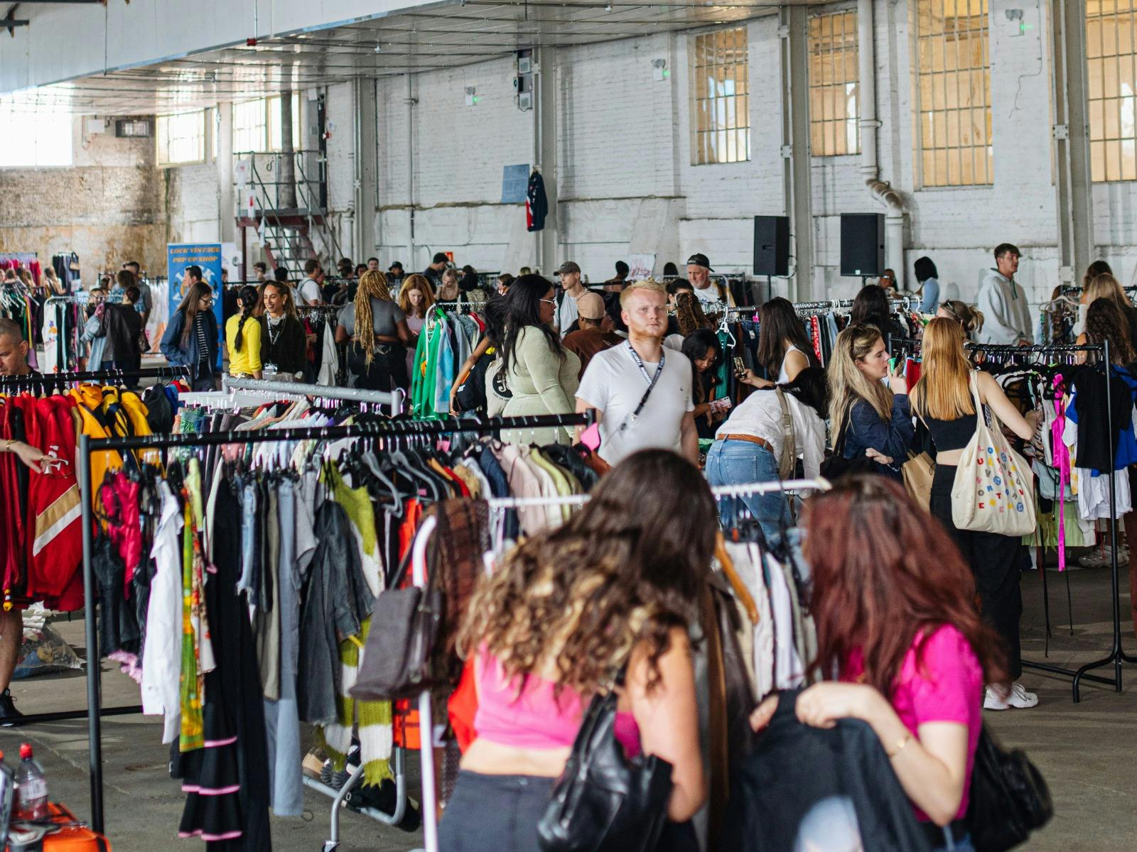 pictured is a view of the market with lots of racks of clothes and people pictured is a view of the market with lots of racks of clothes and people