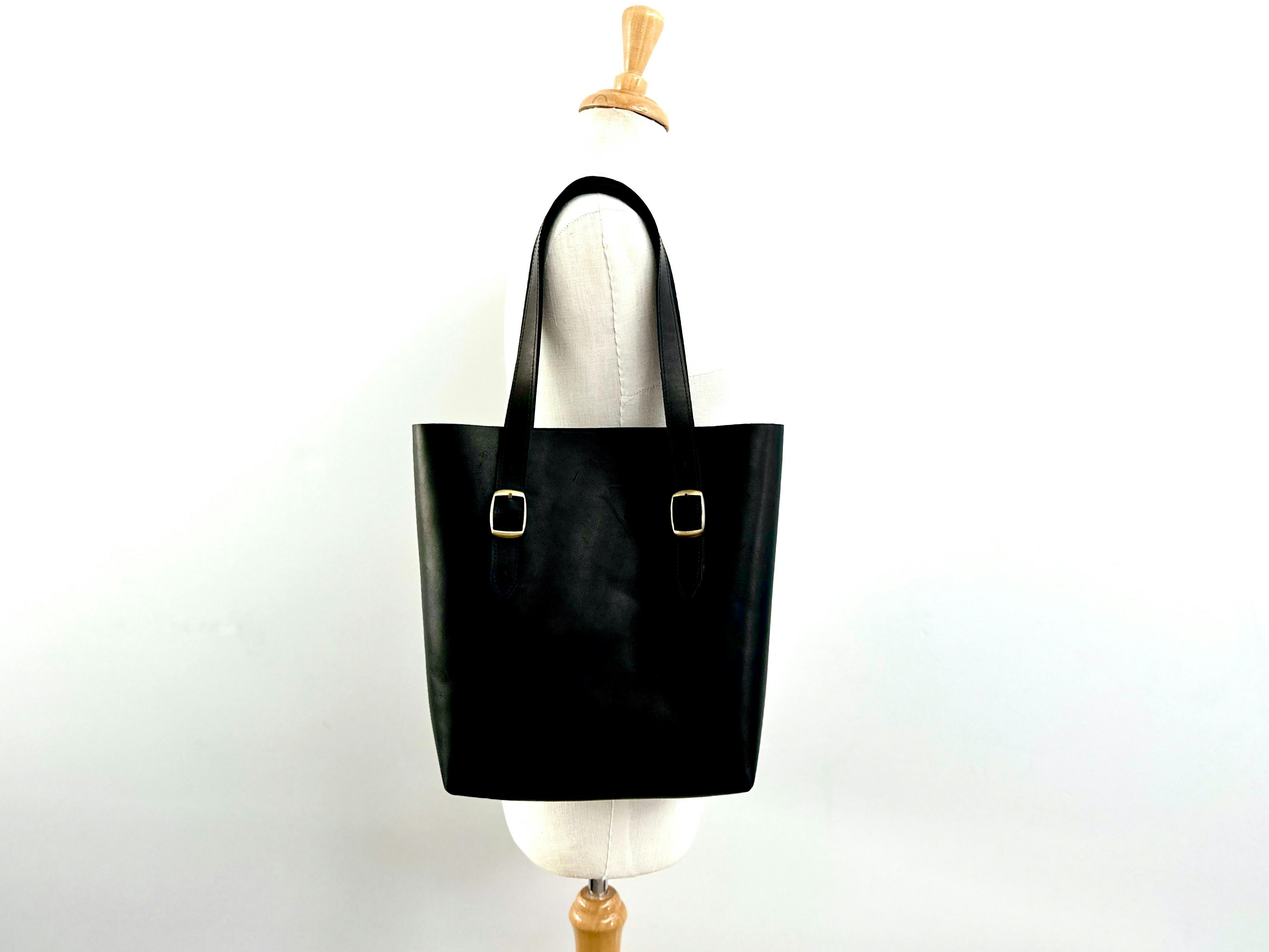 Black leather tote bag with buckle straps displayed on a mannequin against a plain white background
