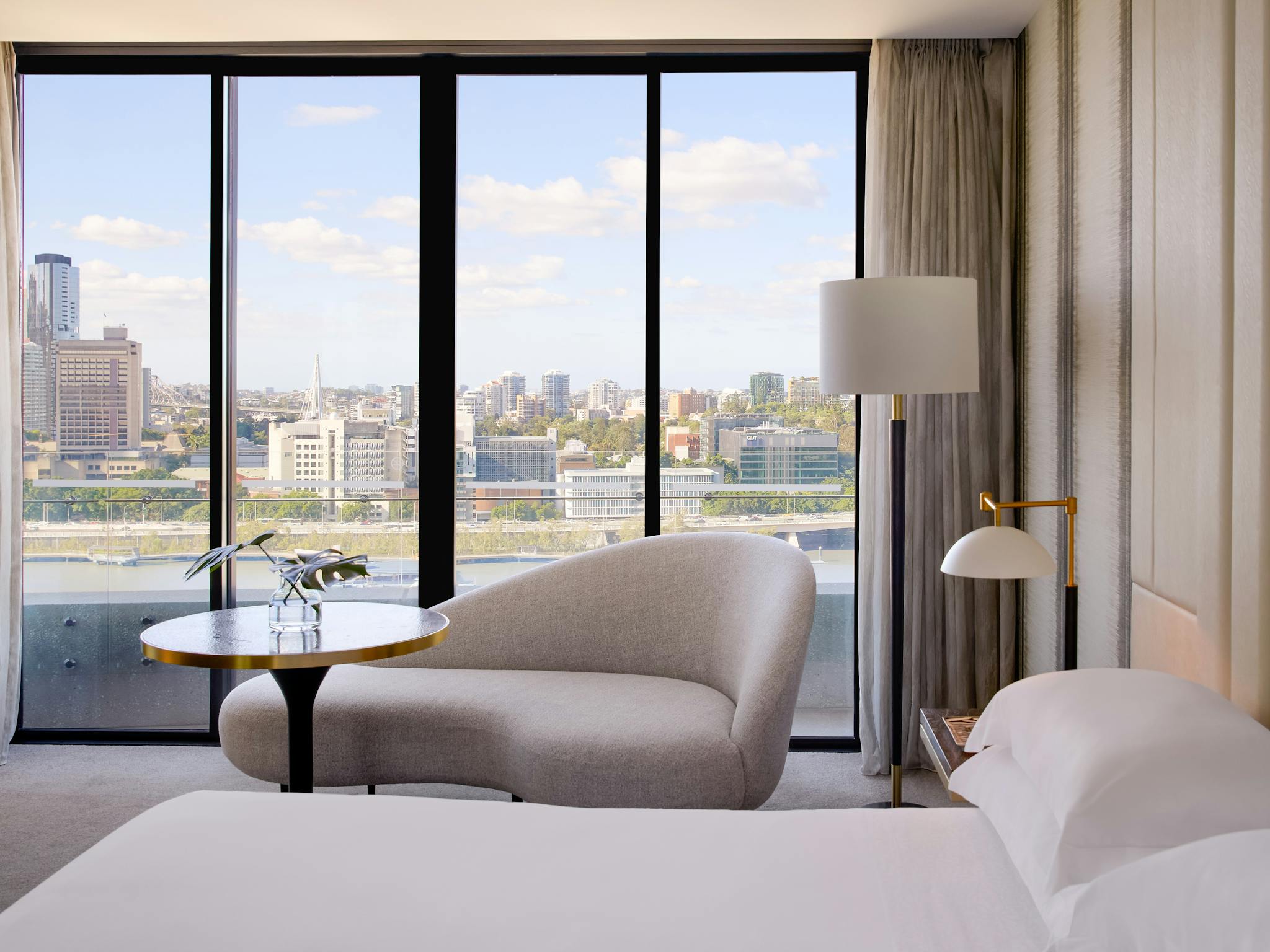 Modern hotel room with curved sofa and table overlooking the Brisbane skyline through tall windows Modern hotel room with curved sofa and table overlooking the Brisbane skyline through tall windows