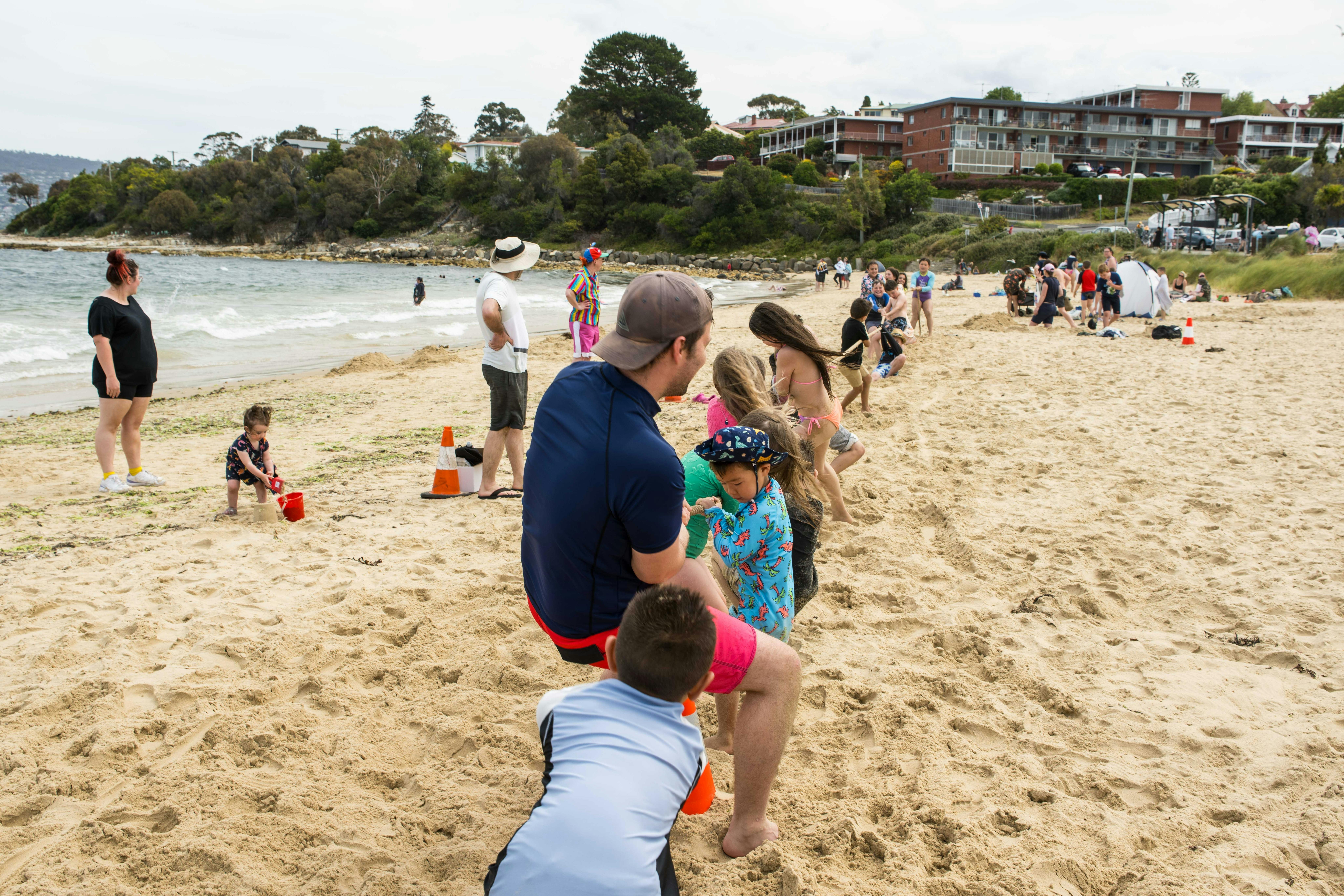 Children play tug of war on a crowded beach.