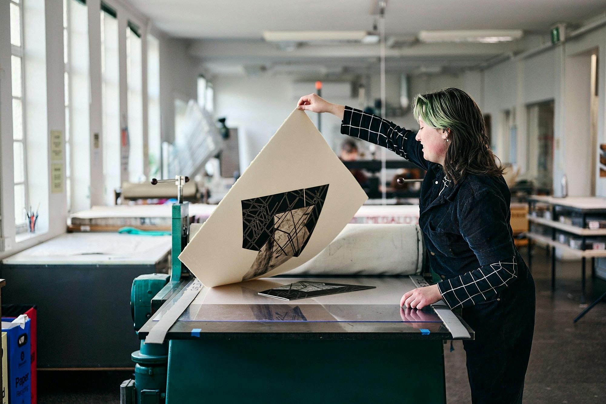 A person pulls a large print on an etching press