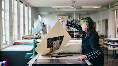 A person pulls a large print on an etching press