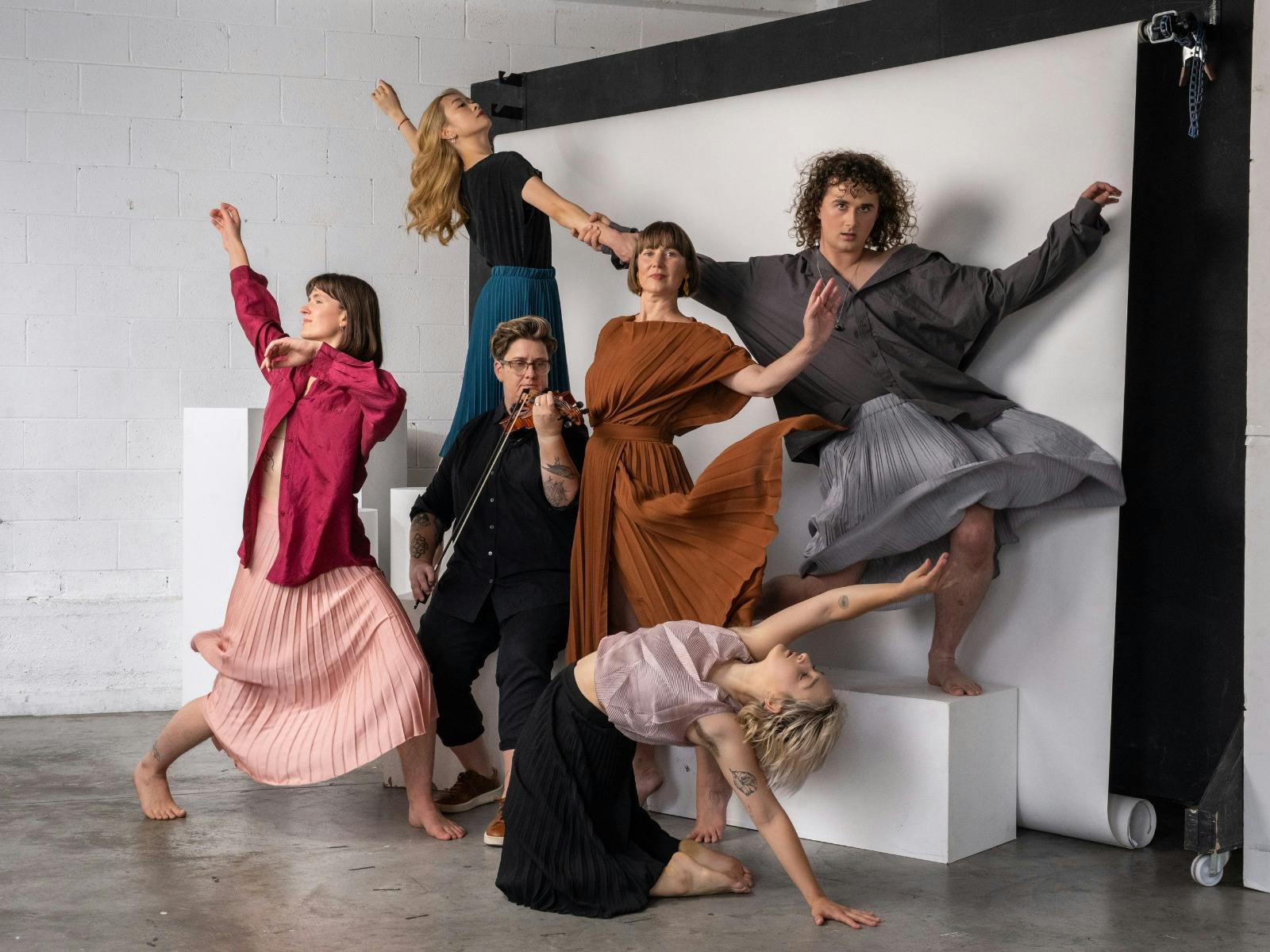A group of dancers stand together, holding poses in a photo studio.