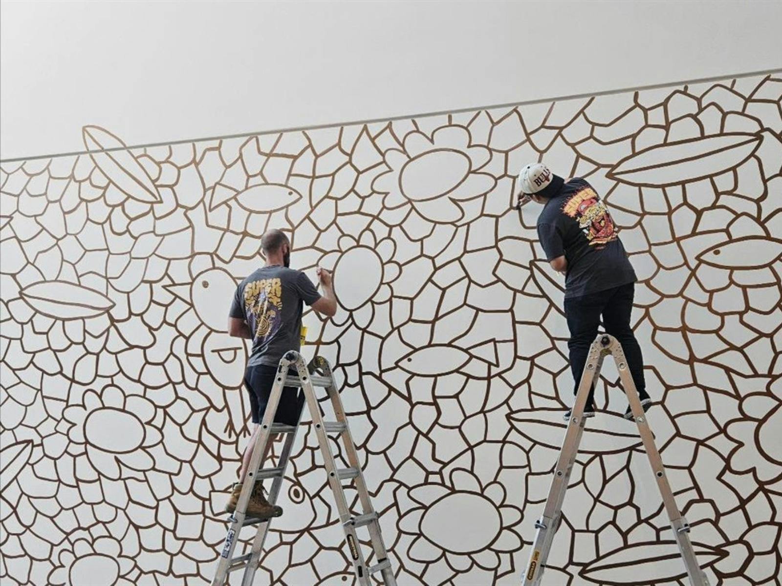 Two installers on ladders painting mural outlines of animals and big circles connecting the elements