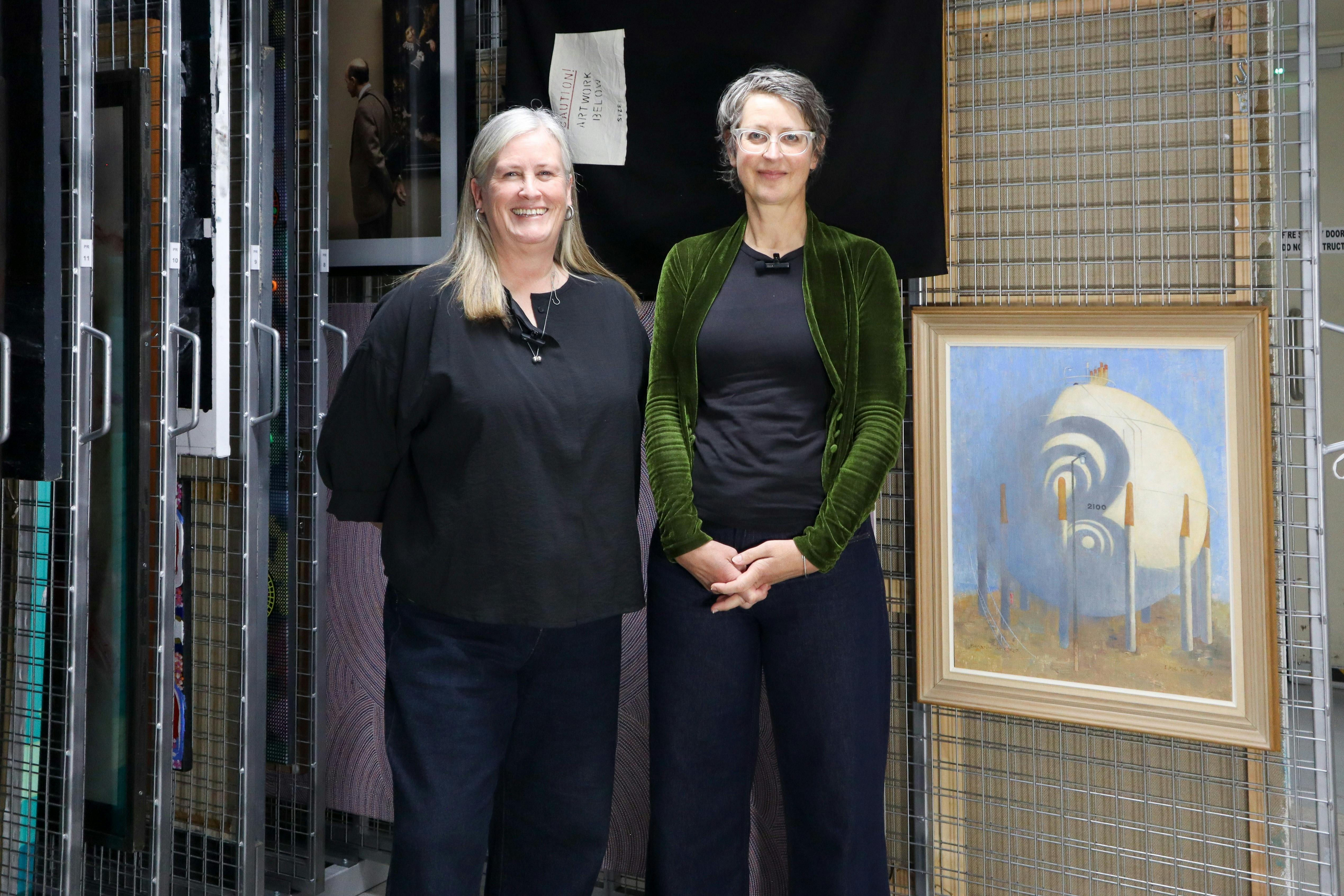 Two females stand next to a painting