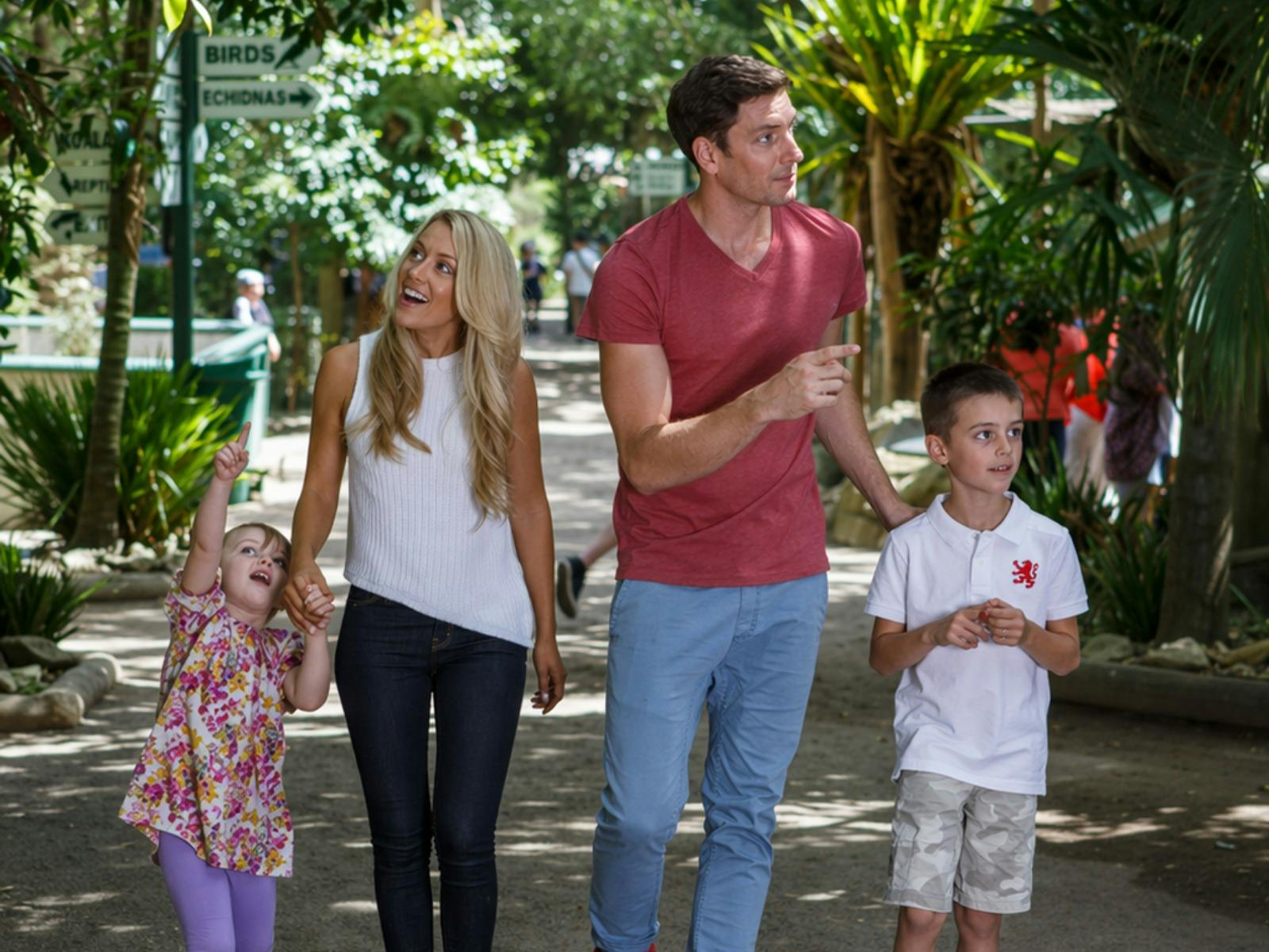 A family of four walks together along a shaded pathway through Featherdale Sydney Wildlife Park.