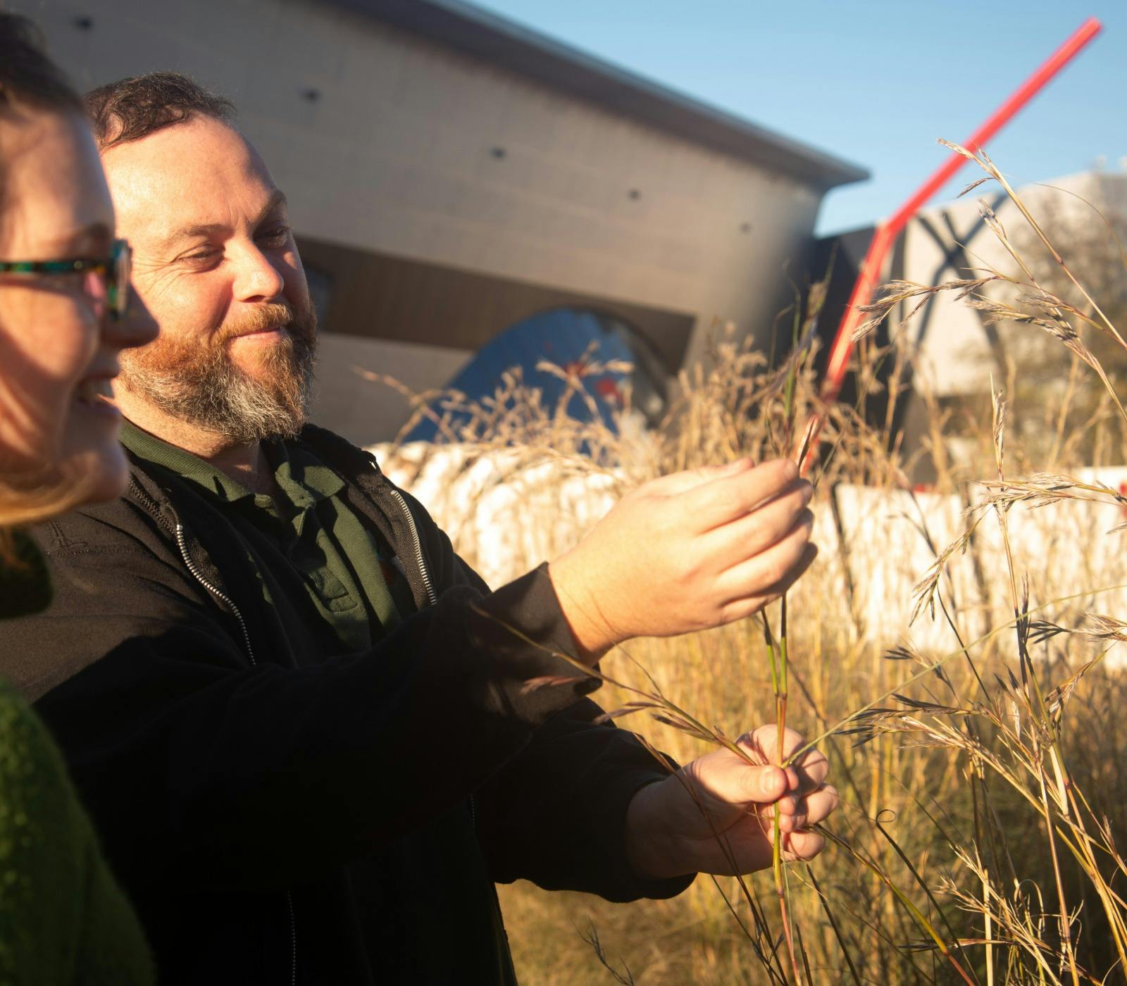 Adam Shipp smiles as he holds native grasses outdoors during a guided cultural experience.