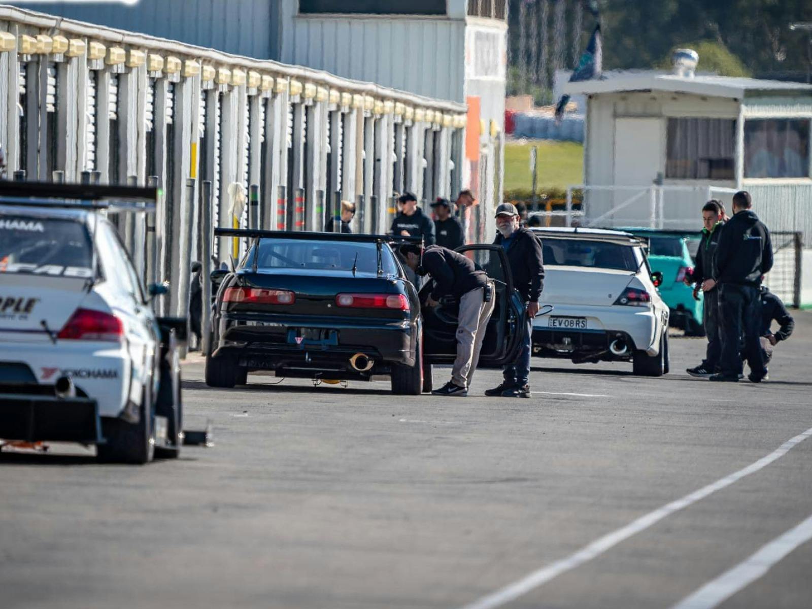 Veiw down pit lane with 3 cars and racing car drivers